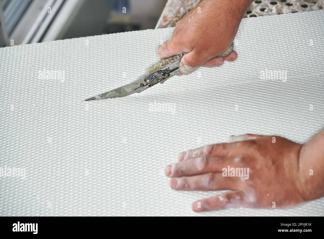 Mann schneidet Wärmeisolierung aus Polystyrolschaum mit altem einziehbarem Universalmesser, Nahaufnahme Stockfoto
