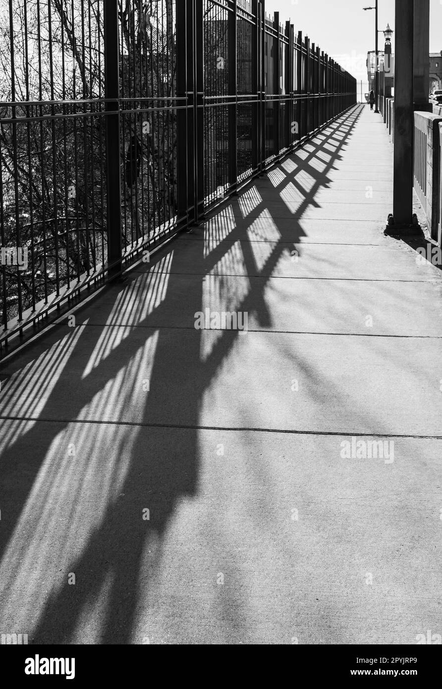 Geländerschatten auf der Brücke. Das Brückengeländer wirft einen Schatten. Abstrakter Brückenschatten. Stadtbild, Straßenfoto, niemand Stockfoto