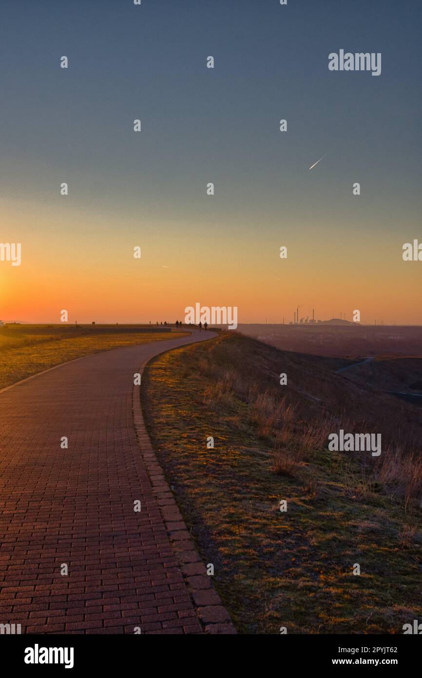 Vertikale Aufnahme eines leeren Gehwegs auf einem Hügel bei Halde Hoheward bei Sonnenuntergang in Deutschland Stockfoto