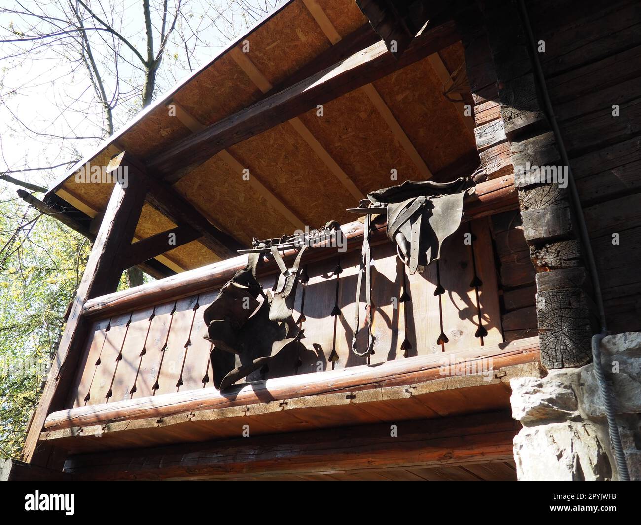 Am Geländer der Holzhausterrasse hängen ein Ledersattel, ein Zaumzeug und Steigbügel. Stanisici, Bijelina, Bosnien und Herzegowina. Pferdesport oder Landwirtschaft und Tierhaltung Stockfoto