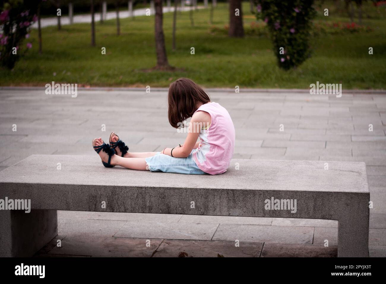 Kleines Mädchen, das allein auf der Bank sitzt Stockfoto