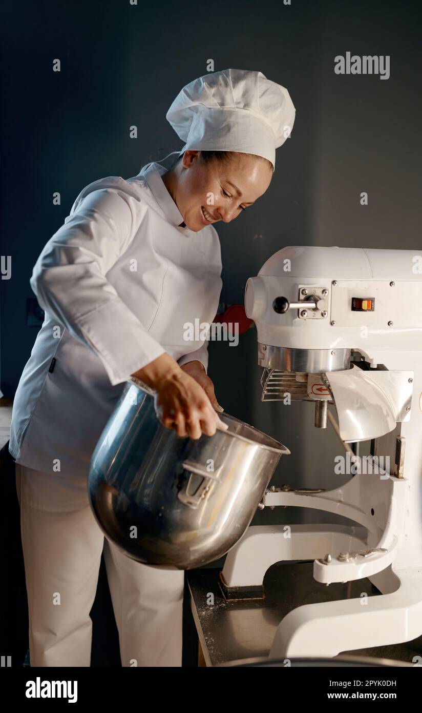 Weibliche Bäckerin in professioneller Küche mit Teigmischer in der Bäckerei Stockfoto