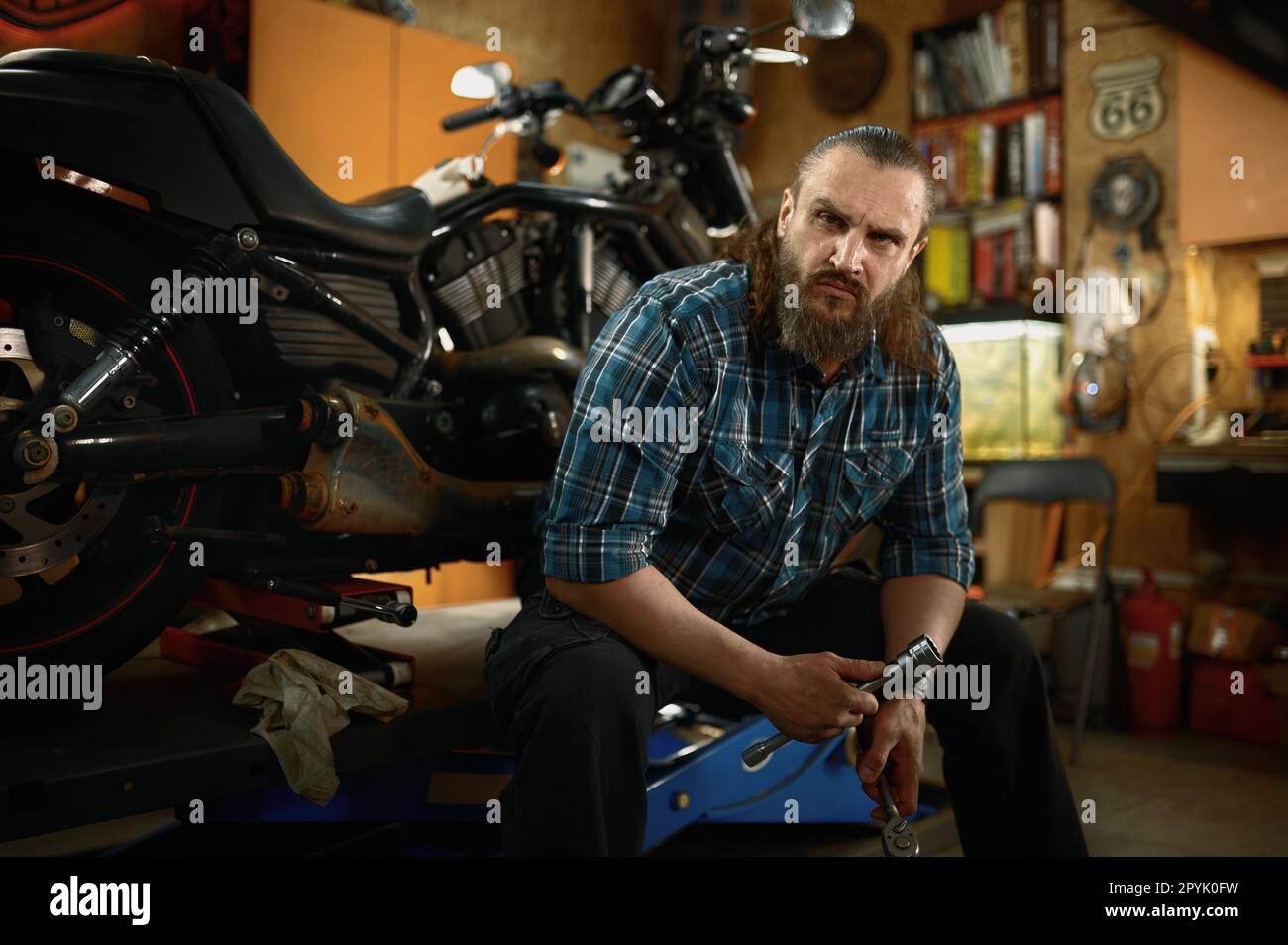 Porträt eines erwachsenen bärtigen Bikers, der in seiner eigenen Garage auf die Kamera schaut Stockfoto