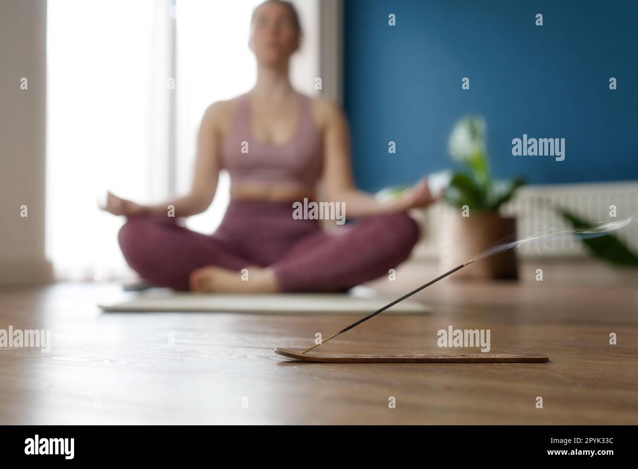 Die Hand der Frauen in Lotus posiert, während sie zu Hause im Morgensonnenlicht am Boden sitzen. Dolly-Shot, Konzept der Entspannung und Meditation mit Weihrauch im Wohnzimmer Stockfoto