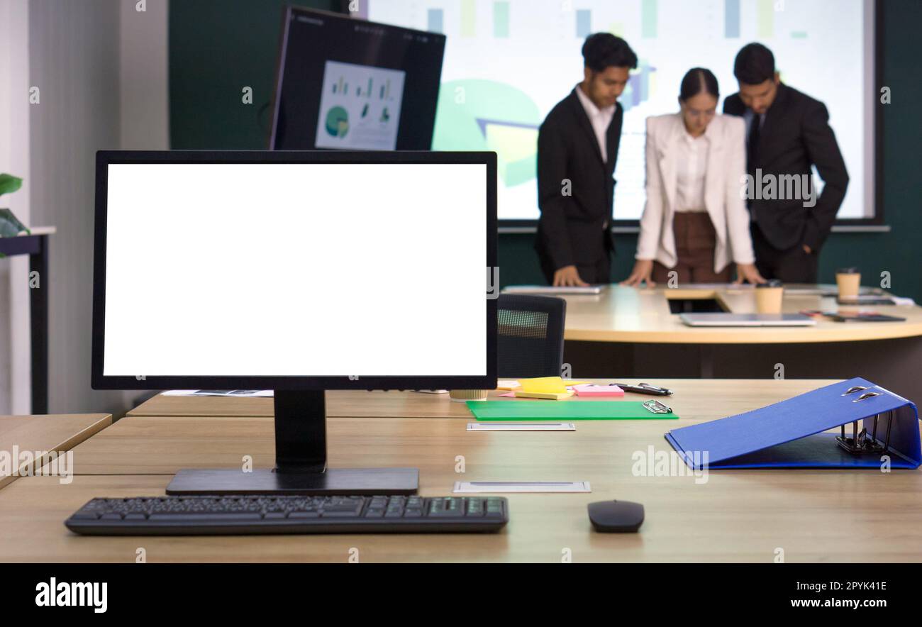 PC-Monitor mit leerem Bildschirm auf dem Schreibtisch. Treffen von Geschäftspartnern im Hintergrund. Arbeitsatmosphäre in einem modernen Büro Stockfoto