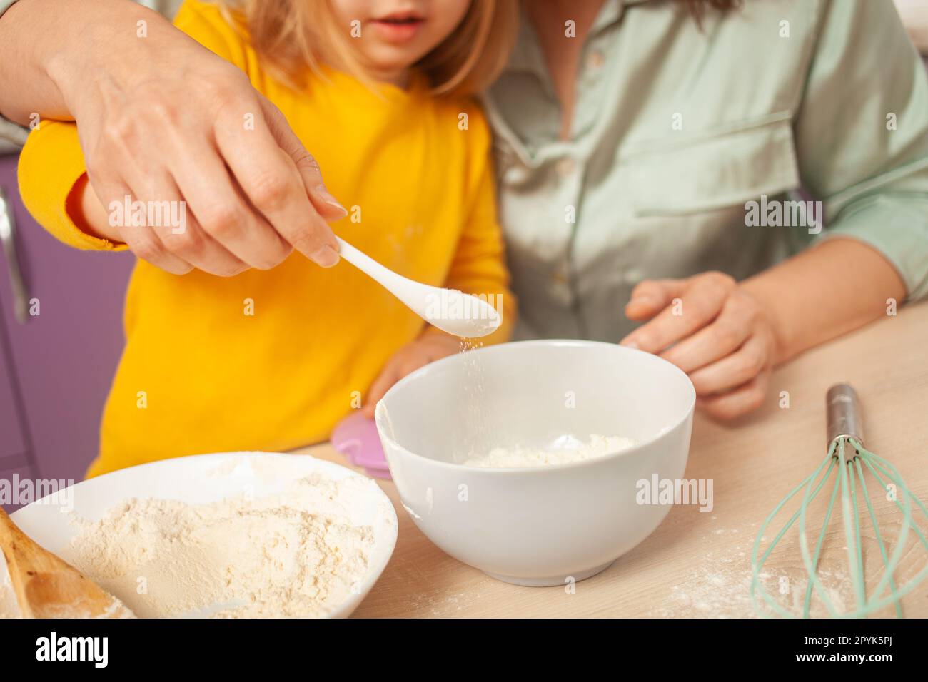 Großmutter und Enkelin bereiten Kuchenteig zu, verbringen Zeit miteinander, Familienbeziehungen, Liebe. Gieße Zucker in eine Tasse. Stockfoto