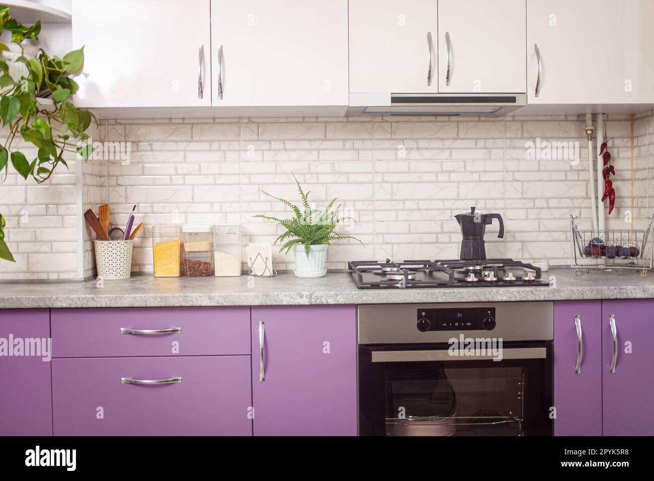 Küche lila, lavendelfarben, weiße Schränke, grüne Blumen, schwarzer Ofen. Hintergrund. Stockfoto