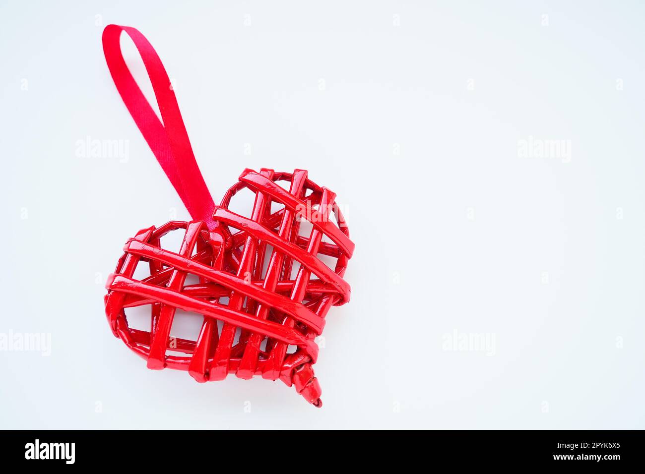 Rotes geflochtenes Herz mit Seidenband auf weißem Hintergrund. Valentinstag. Kopierraum. Ein hübsches Souvenir - eine schräg angebrachte Anhänger. Stockfoto