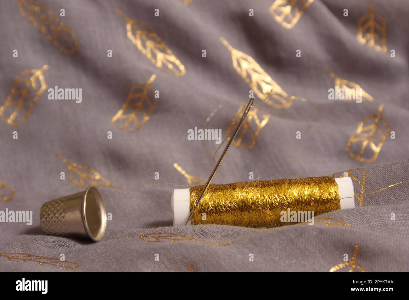 Spule mit Gewinde in Metallic Gold auf grauem und goldenem Stoff Stockfoto