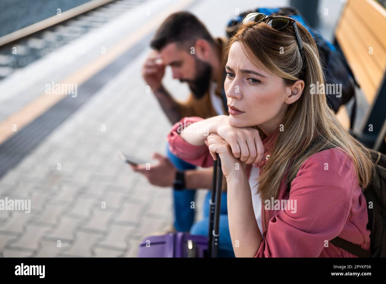 Ein ängstliches und müdes Paar, das am Bahnhof sitzt und auf die Ankunft des Zuges wartet. Stockfoto