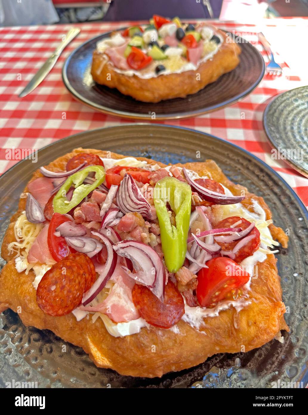 Langos, Pizza nach ungarischer Art auf einem Teller, gebratenes Gebäck, geriebener Käse, Sauerrahm, Speck, Salami, Zwiebeln und Petersilie Stockfoto