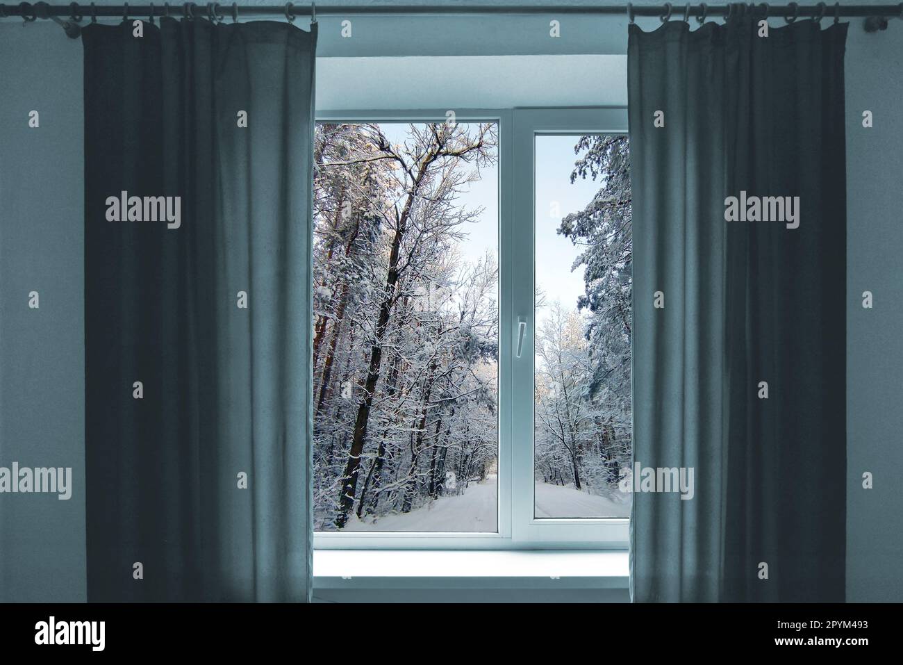 Fenster in einem Zimmer mit Blick auf die Winterlandschaft. Zimmer mit Fenster. Fenster mit grauen Vorhängen. Kaltes und verschneites Wetter vor dem Fenster. Stockfoto