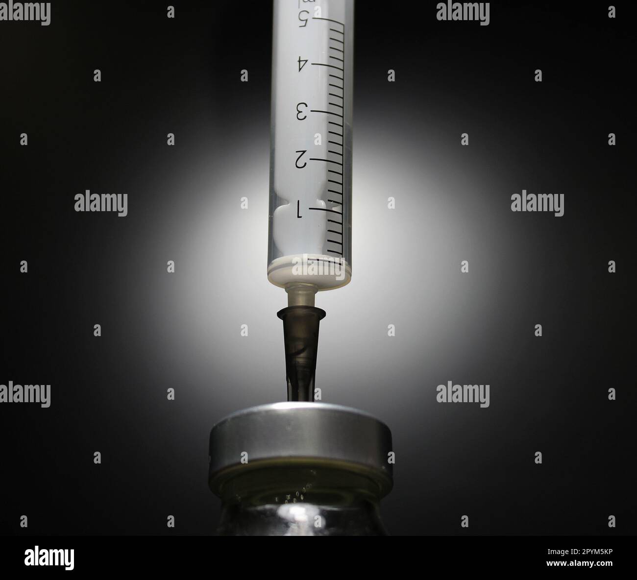 5ml Einmalspritze injiziert Nadel in eine Flasche mit Impfstoff, der auf schwarzem Foto isoliert wurde Stockfoto