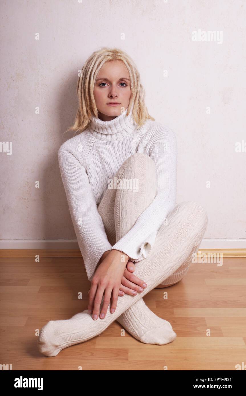 Einsame Frau tragen rollkragen pullover und overknee Socken sitiing auf, lehnte sich gegen die Wand Stockfoto