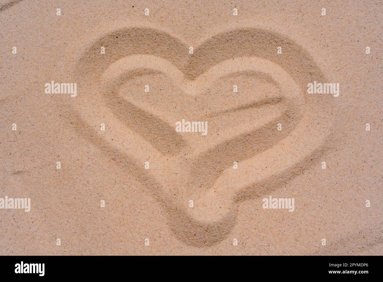 Makro-Nahaufnahme der Sandtextur mit einem Finger-gezogenen Herz. Hintergrund aus feinem Sand. Fotos in hoher Qualität Stockfoto