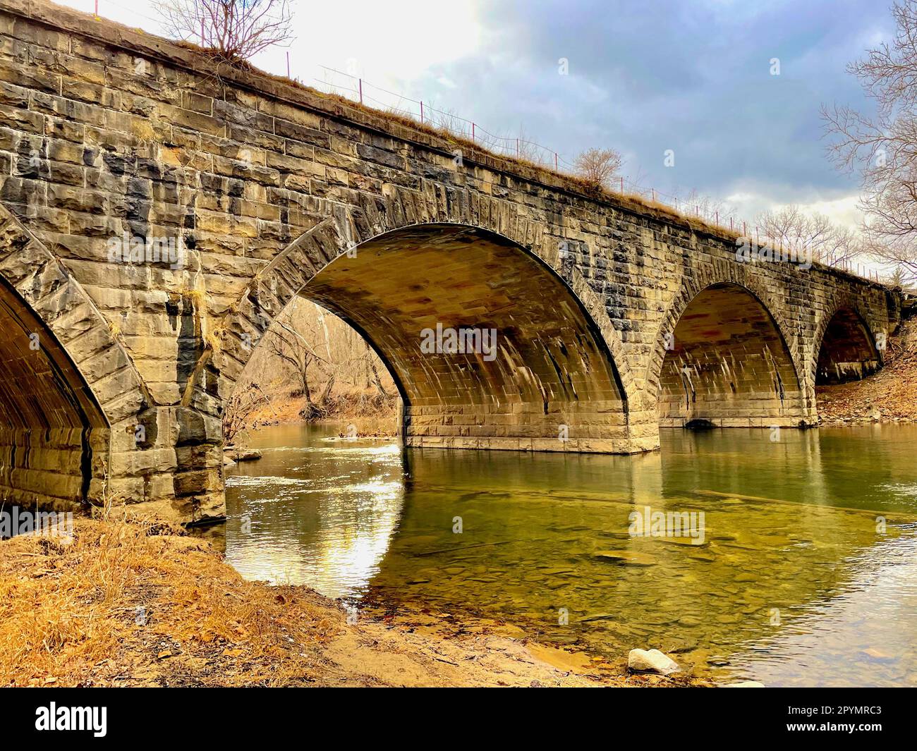 Der Cacapon River fließt unter einer historischen Steinbrücke, die von Güterzügen und Amtrak-Zügen in der Nähe des Potomac River genutzt wird. Stockfoto