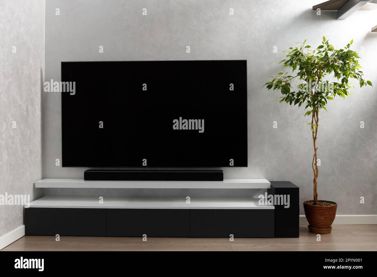 Teil des Wohnzimmers mit Fernseher an der Wand, HiFi-Ausstattung, Soundbar,  grauem Schrank und einer großen Innenblume. TV- und Musiksystem  Stockfotografie - Alamy
