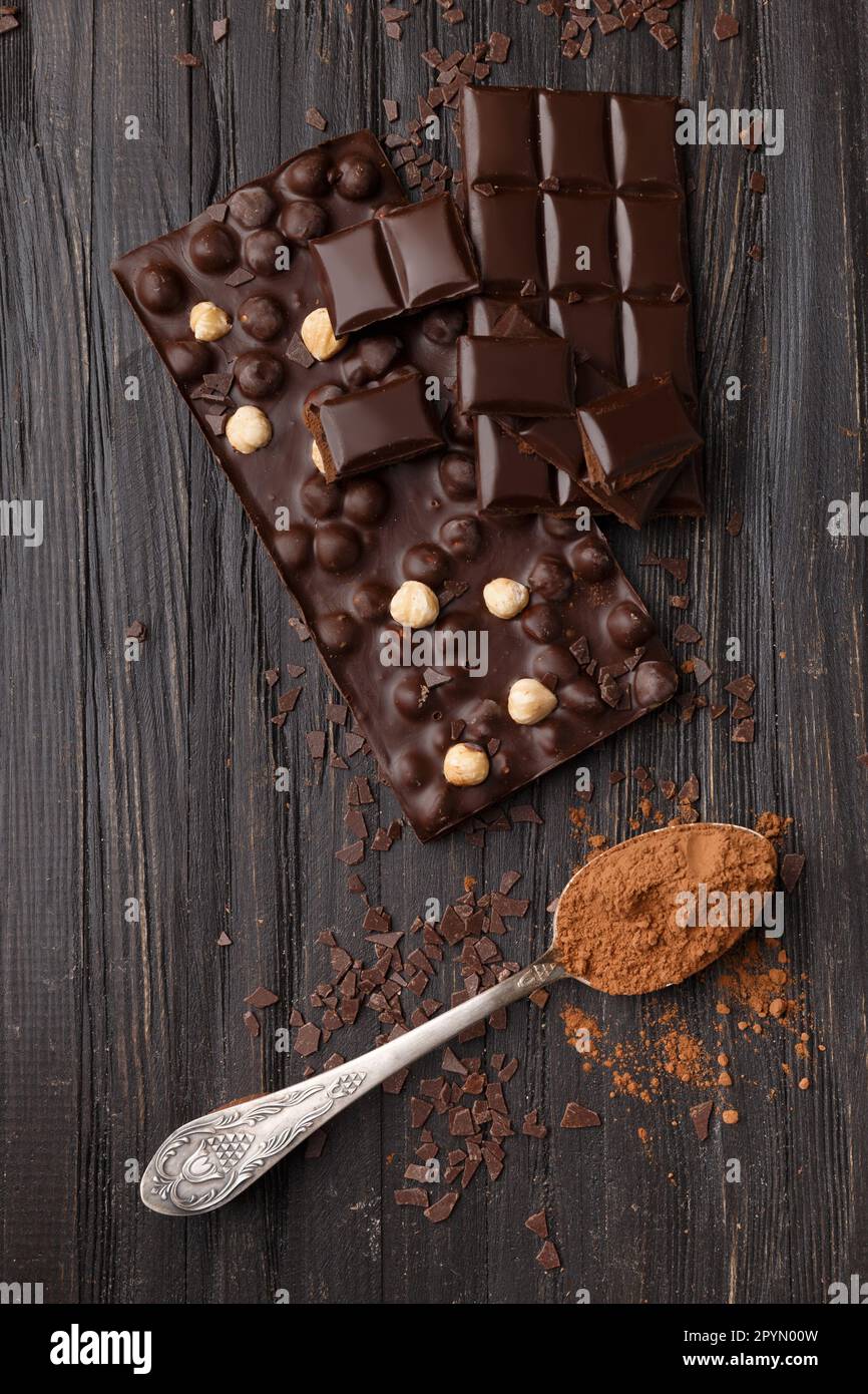 Handgemachte Schokolade mit Haselnüssen, dunklen Schokoladenstücken, Kakao in einem alten Löffel auf einem dunklen Holzhintergrund mit Blick von oben. Schokoladenvariante. Stockfoto