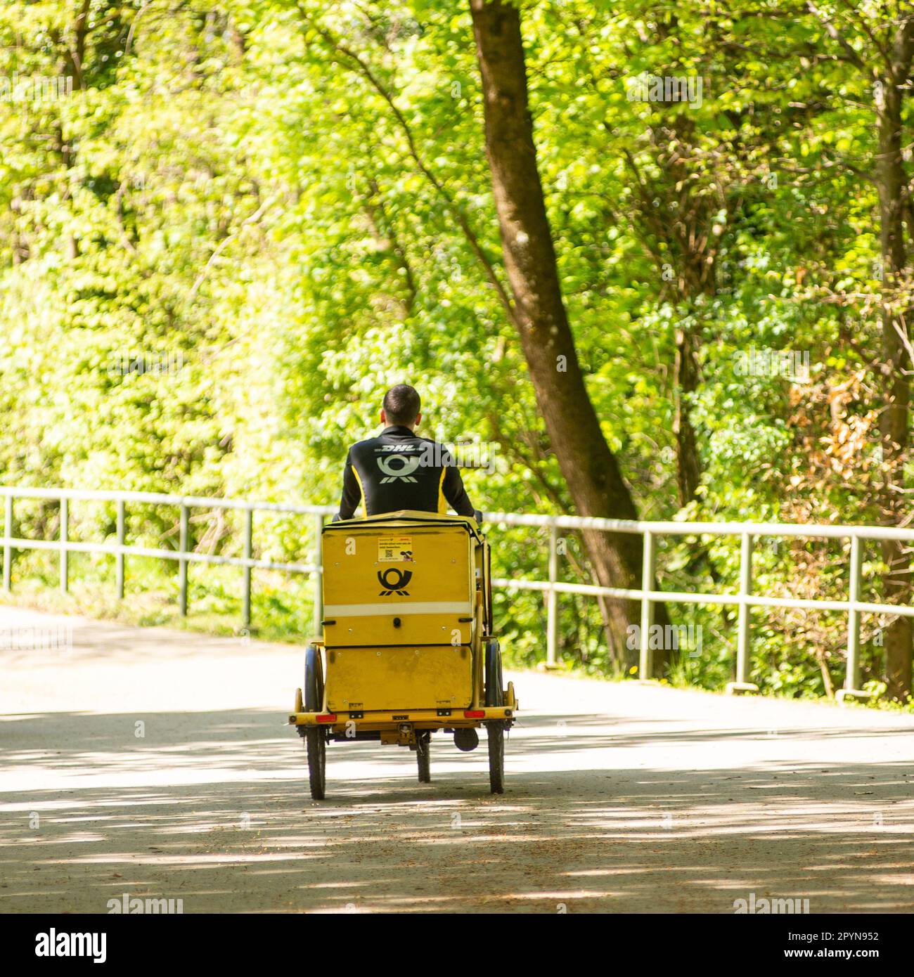 Ein Postbote auf einem Trycicle reitet durch einen Park mit Post Stockfoto