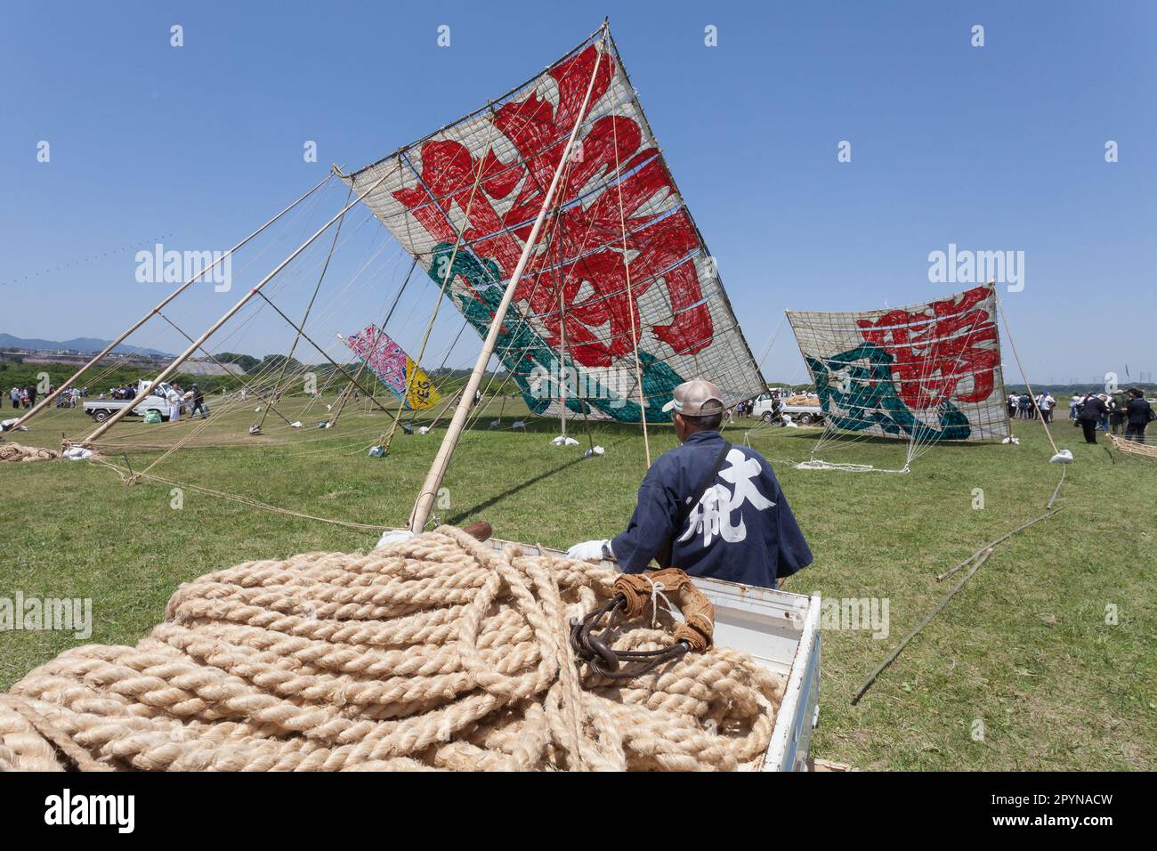 Ein kleiner Kleinbus mit Seilen vor großen Drachen auf dem Sagami Giant Kite Festival (Sagami-no-Oodako) Sagamihara. Das Sagami Giant Kite Festival begann in den 1830er Jahren als Ergänzung zum Children's Festival, das am 5. Mai in japan gefeiert wird. Mit der Zeit sind die Drachen, die aus Bambus und handgemachtem Papier bestehen, größer geworden. Die größten Drachen, die während dieses Festivals vom Flussufer der Sagami geflogen wurden, sind etwa 15 Meter lang und können über 900 Kilogramm wiegen. Ein Team von 80 bis 100 Personen braucht sie, um sie in die Luft zu jagen. Stockfoto