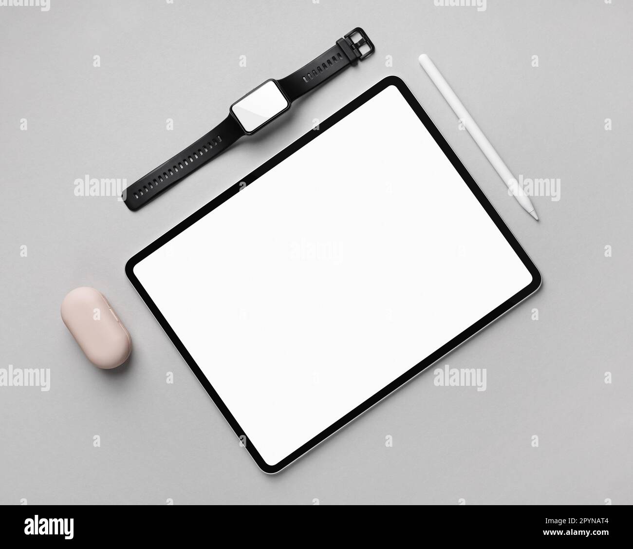 Tablet-Computer mit weißem Bildschirm, Fitnessarmband und Eingabestift auf grauem Papierhintergrund. Draufsicht. Flach verlegt. Stockfoto