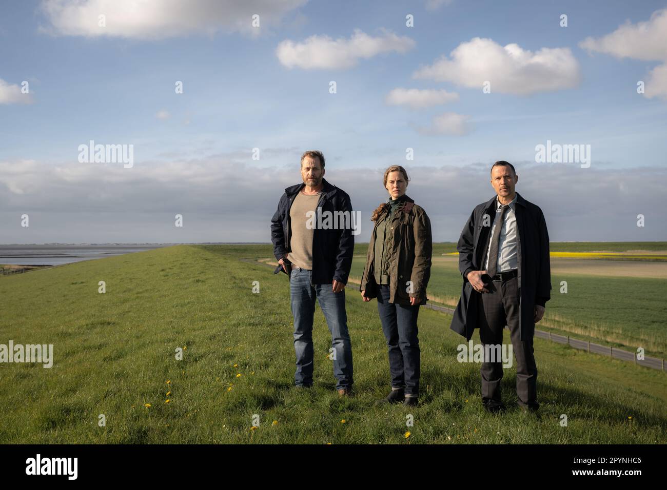 Norden, Deutschland. 03. Mai 2023. Die Schauspieler Christian Erdmann (l-r), Picco von Groote und Barnaby Metschurat stehen auf dem Deich während einer Nachstellung einer Filmszene während eines exklusiven Fototermins als Teil der Dreharbeiten für die ZDF-Serie „Ostfrieslandkrimi“. Kredit: Mohssen Assanimoghaddam/dpa/Alamy Live News Stockfoto