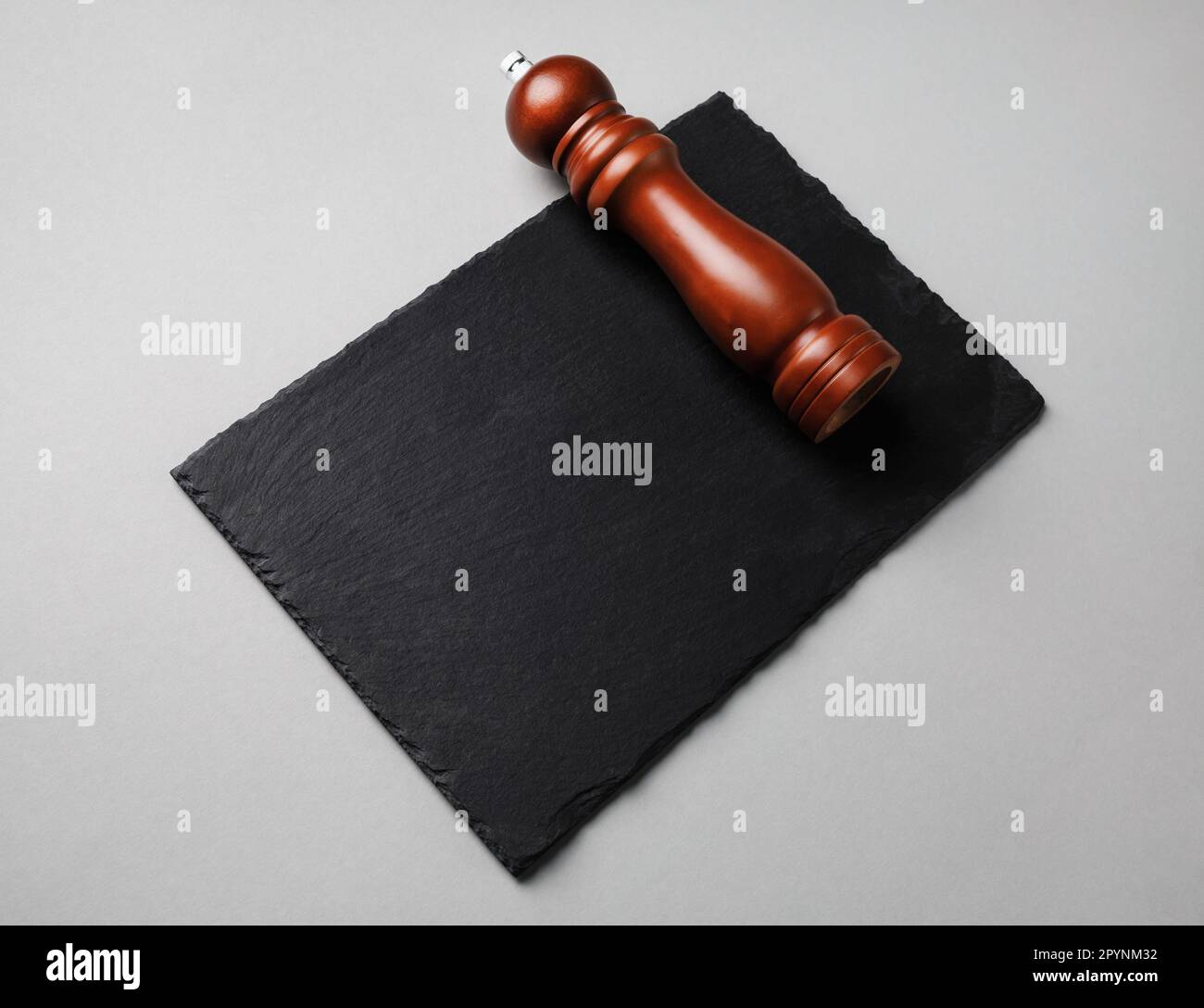 Pfeffermühle und schwarze Steinschieferplatte auf grauem Papierhintergrund. Stockfoto