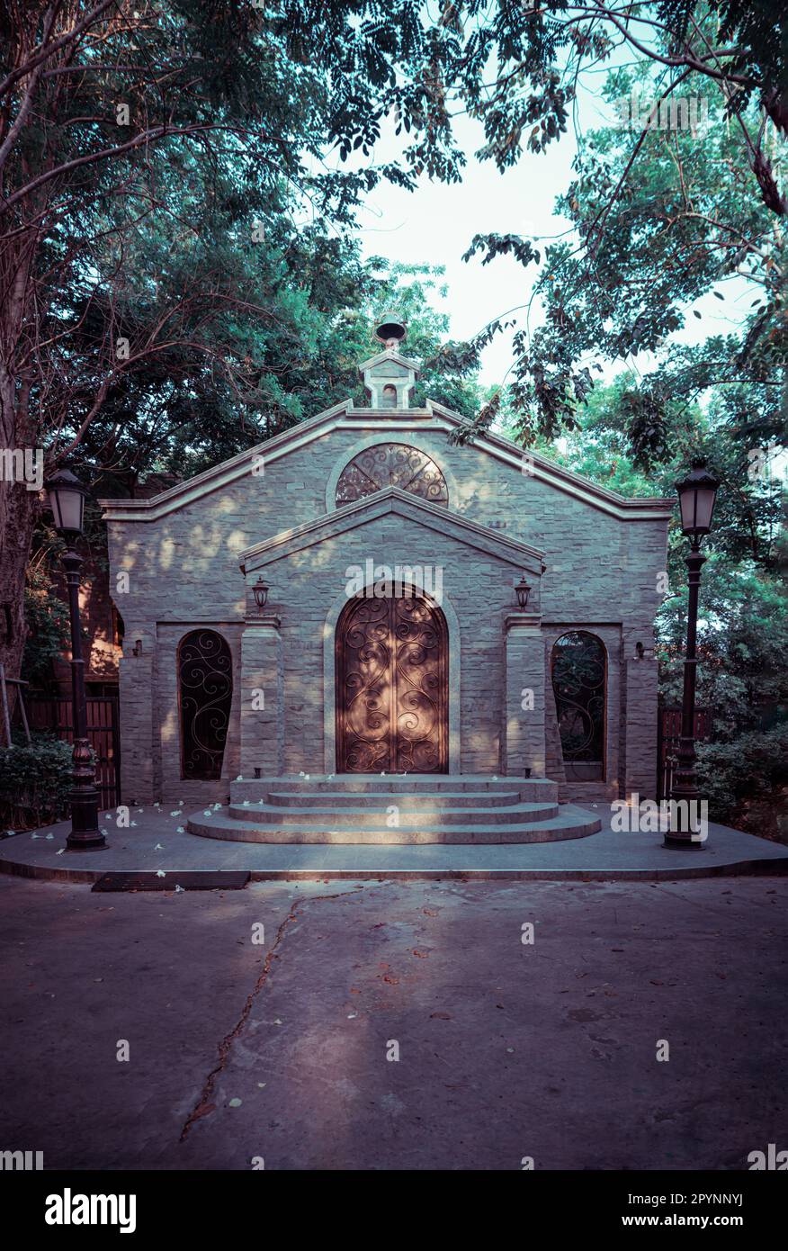 NakhonSawan, Thailand - 23. April 2023 - Antike eiserne Bogentür an einer Ziegelsteinwand in einem historischen Backsteingebäude, umgeben von Straßenlaternen Stockfoto