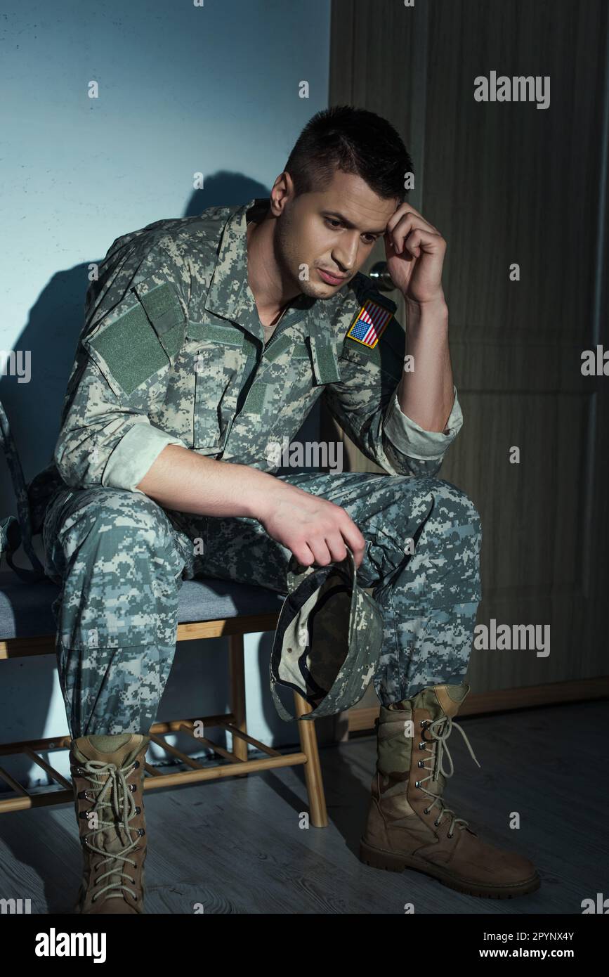 Frustrierter amerikanischer Militärveteran in Uniform, der nachts zu Hause im Flur sitzt, Börsenbild Stockfoto