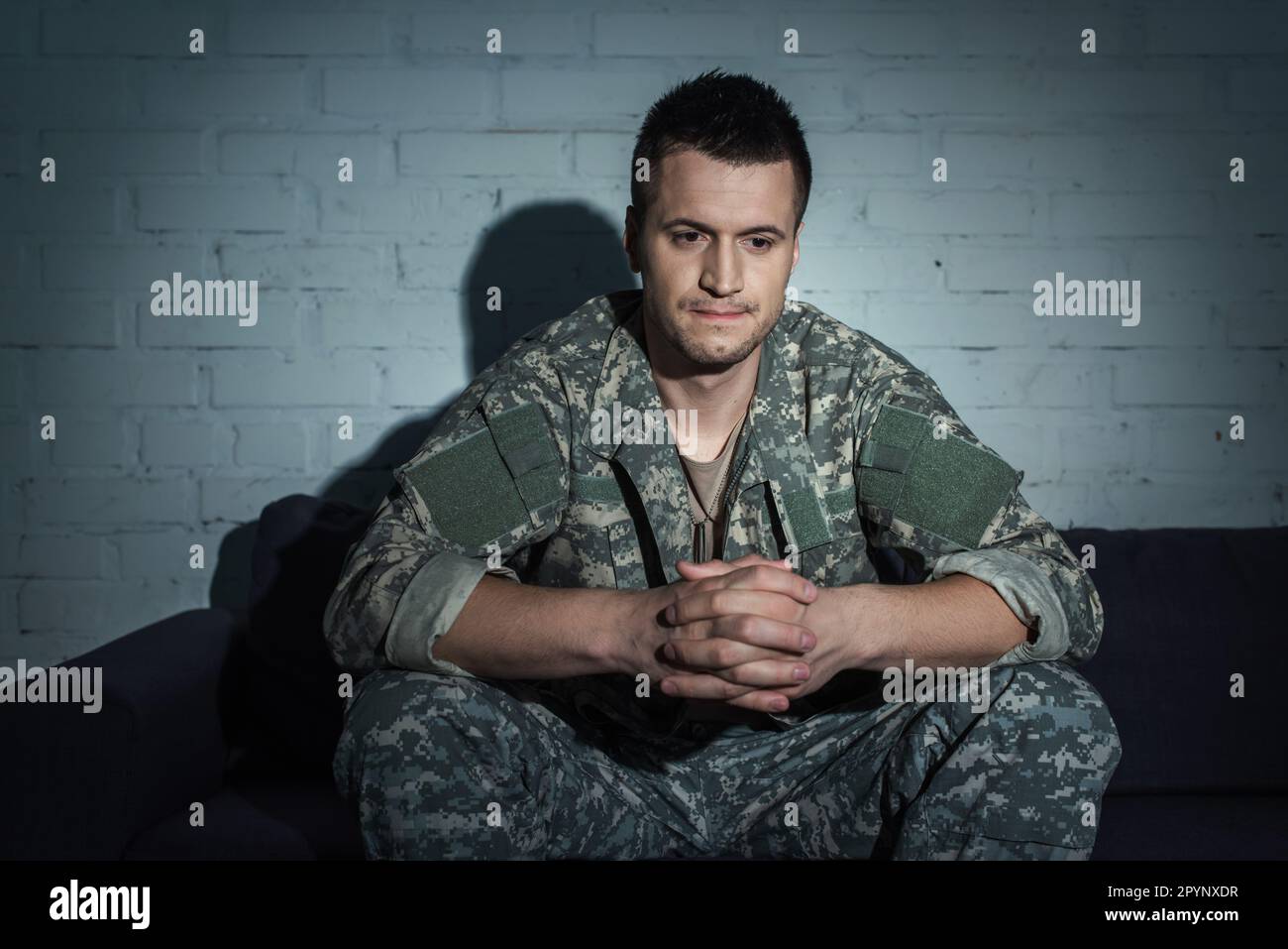 Frustrierter Soldat mit psychischen Störungen, der nachts zu Hause auf der Couch sitzt, Stockbild Stockfoto