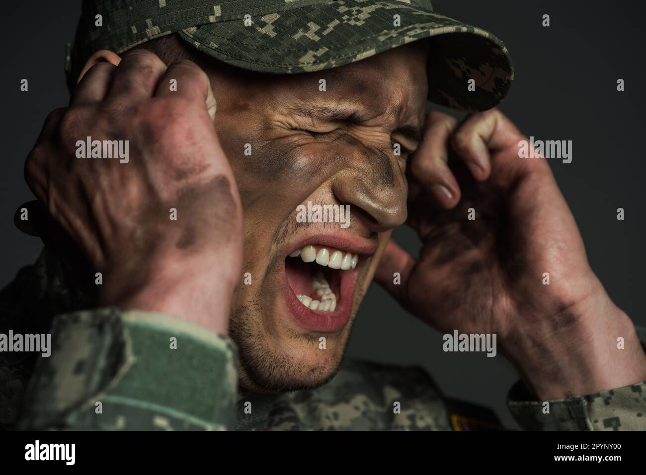 Militärmann mit Dreck im Gesicht, schreiend, während er an posttraumatischer Belastungsstörung leidet, isoliert auf grauem Stockbild Stockfoto