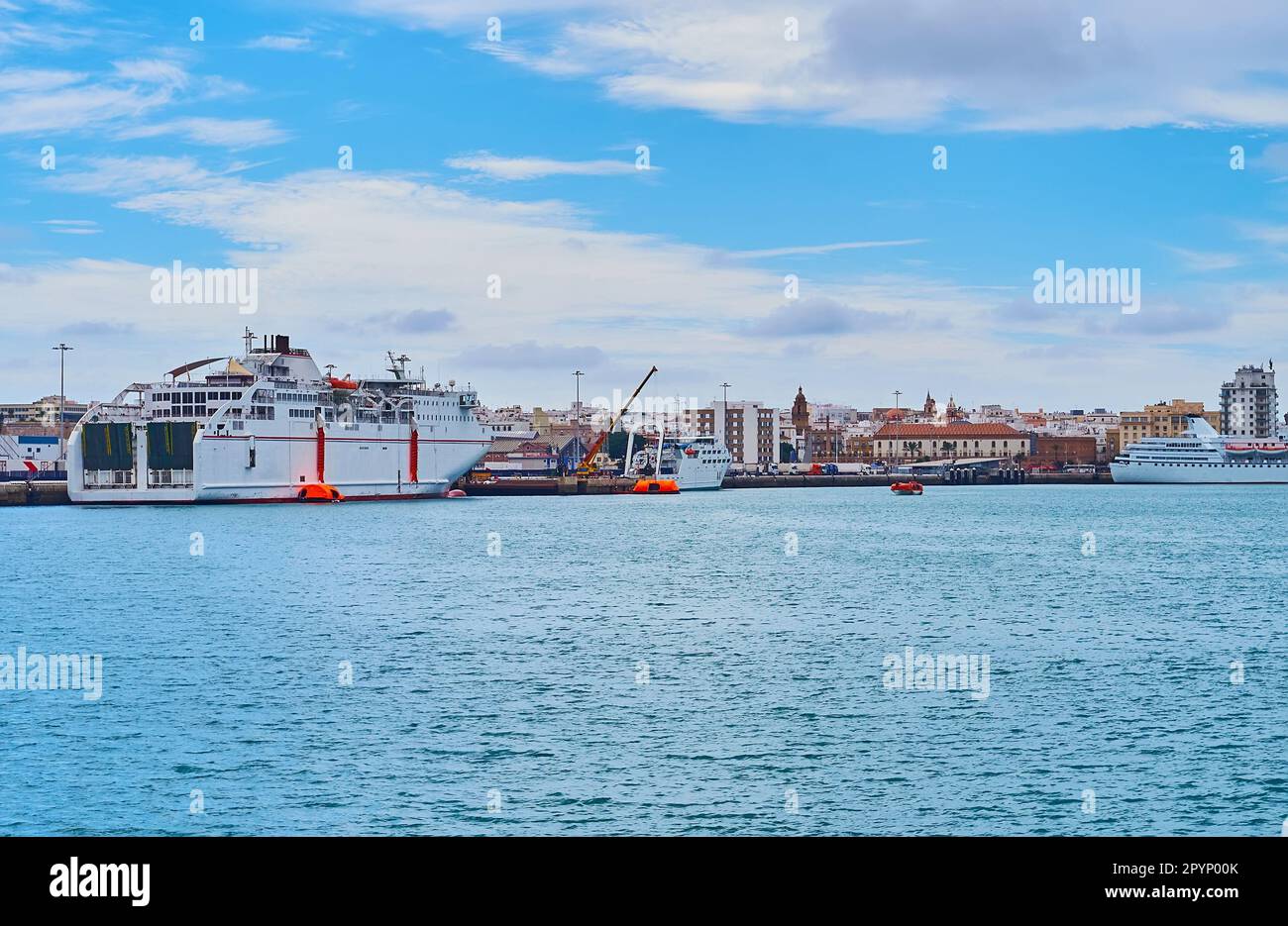 Die Fähre fährt in den Hafen von Cadiz mit einem festsitzendem Schiff und Gebäuden der Altstadt im Hintergrund, Cadiz, Spanien Stockfoto