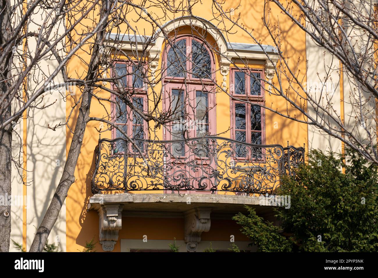 Der alte rustikale schmiedeeiserne Balkon ist von Bäumen umgeben Stockfoto