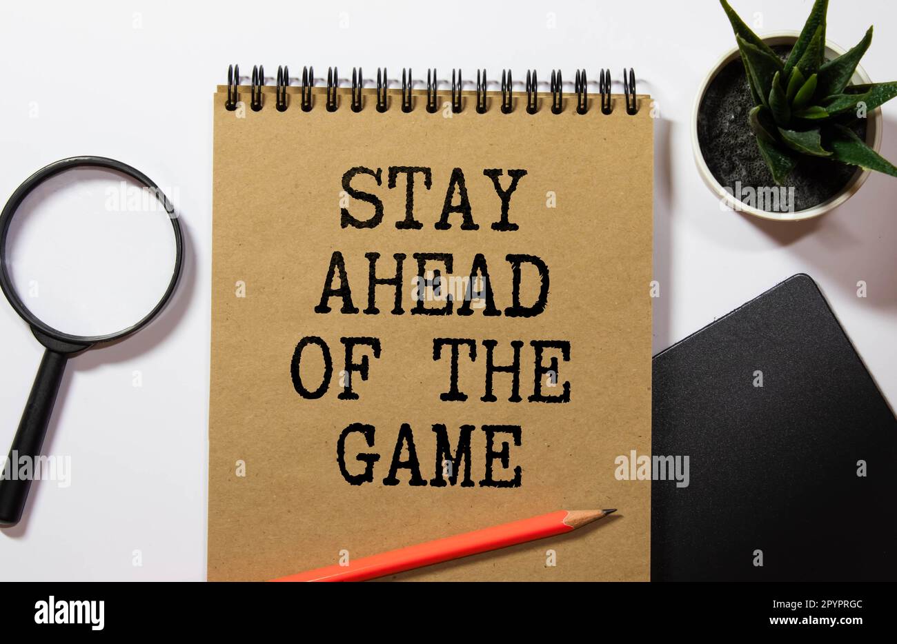 Eine weiße Karte mit dem Text „Stay Ahead the Game“ steht auf einem Clip für Unterlagen auf dem Tisch vor dem Hintergrund von Büchern. Unschärfe-Effekte Stockfoto
