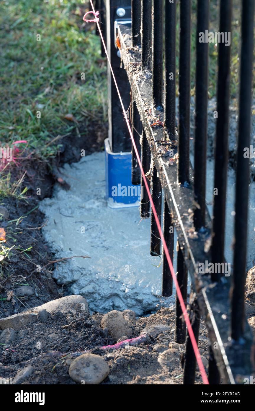 Es wurde eine rosafarbene Schnur für Baumeister verlegt, um sicherzustellen, dass die Zauntafel gerade ist. Der Beton, der den Zaun ost hält, ist noch nass. Stockfoto