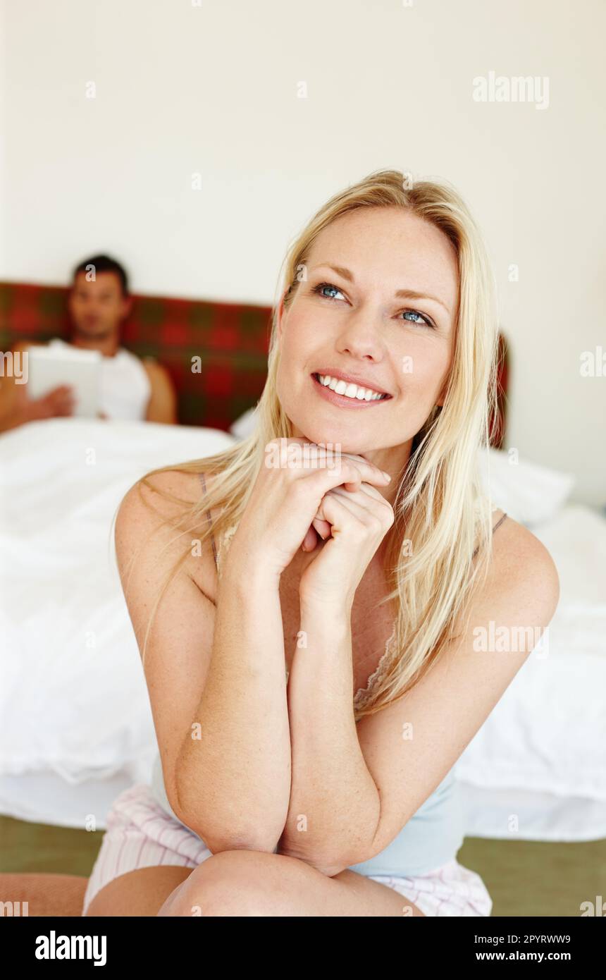 Einen faulen Sonntag. Porträt einer hübschen Frau, die am Rand des Bettes sitzt, mit ihrem Freund, der im Bett sitzt und seinen Touchscreen liest. Stockfoto