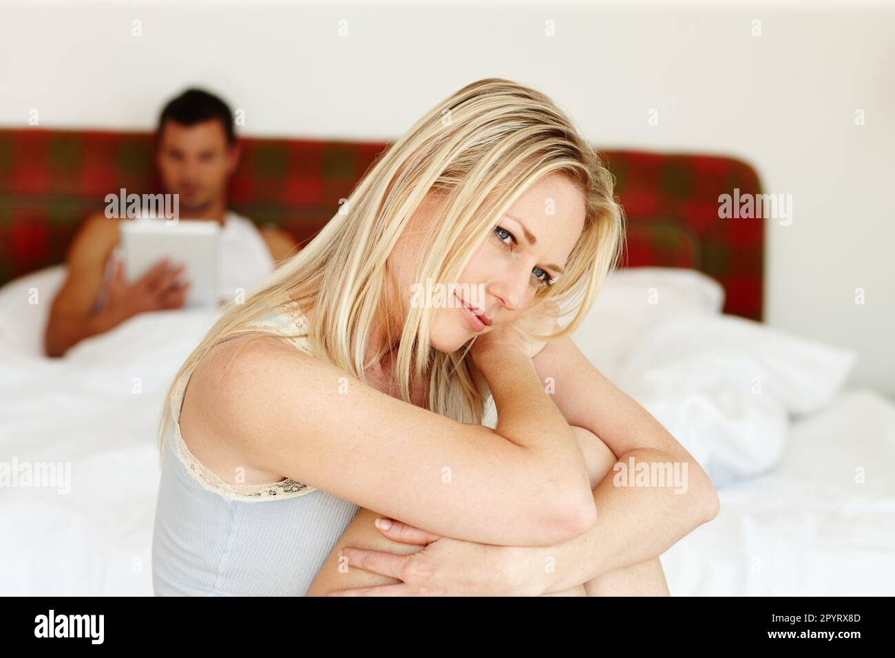 Ein Moment der Besinnung. Porträt einer verletzlich aussehenden Frau, die am Rand des Bettes sitzt, mit ihrem Freund im Hintergrund. Stockfoto