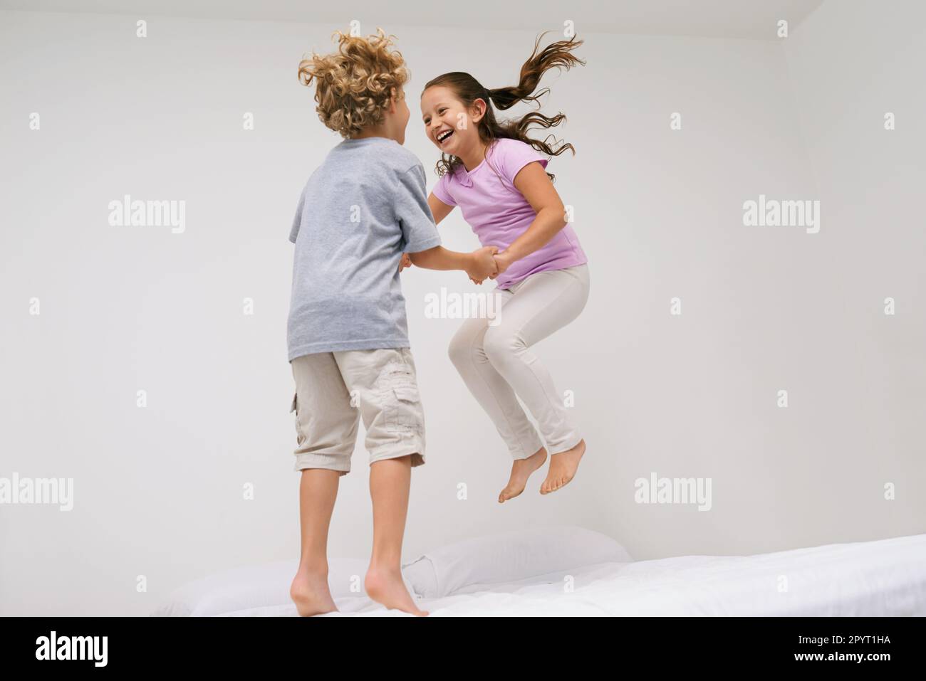 Fröhliches Kichern. Zwei kleine Kinder, die zusammen auf ein Bett springen. Stockfoto