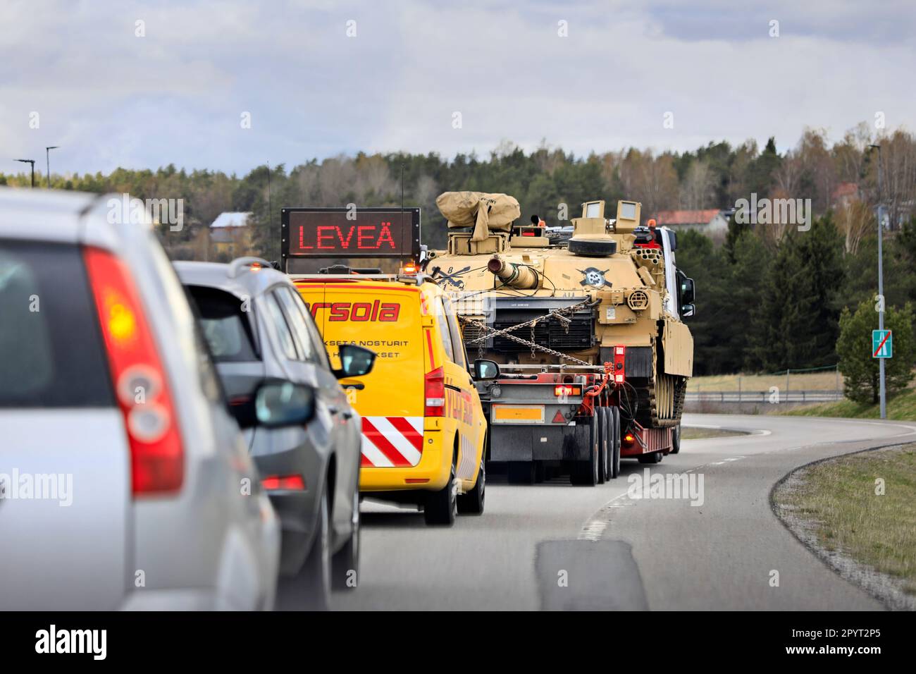 LKW transportiert amerikanischen M1 Abrams Militärtank auf einem Tieflader auf einer Autobahnrampe, unterstützt von einem Begleitfahrzeug. Salo, Finnland. 28. April 2023. Stockfoto
