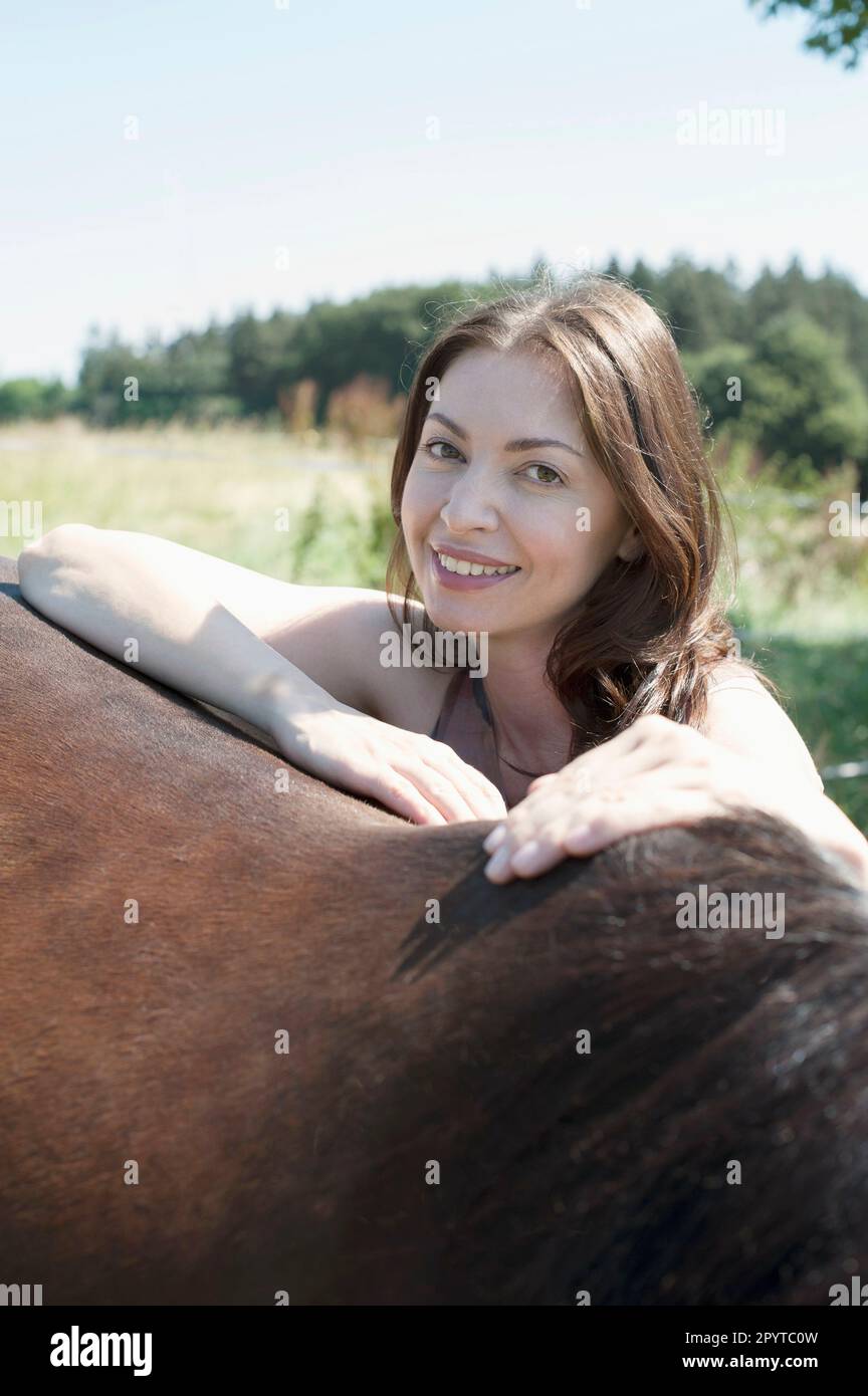 Porträt einer erwachsenen Frau, die sich auf den Rücken ihres braunen Pferdes lehnt und lächelt, Bayern, Deutschland Stockfoto