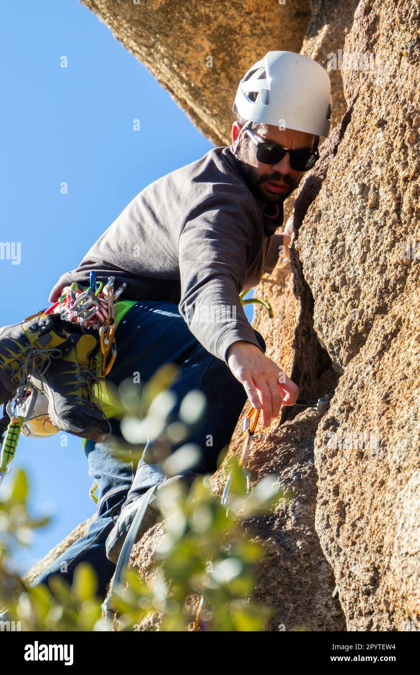 Junger Erwachsener bereitet seinen nächsten Zug vor, während er eine Granitmauer in Torrelodones, Madrid, erklimmen möchte. Extremsportkonzept Stockfoto