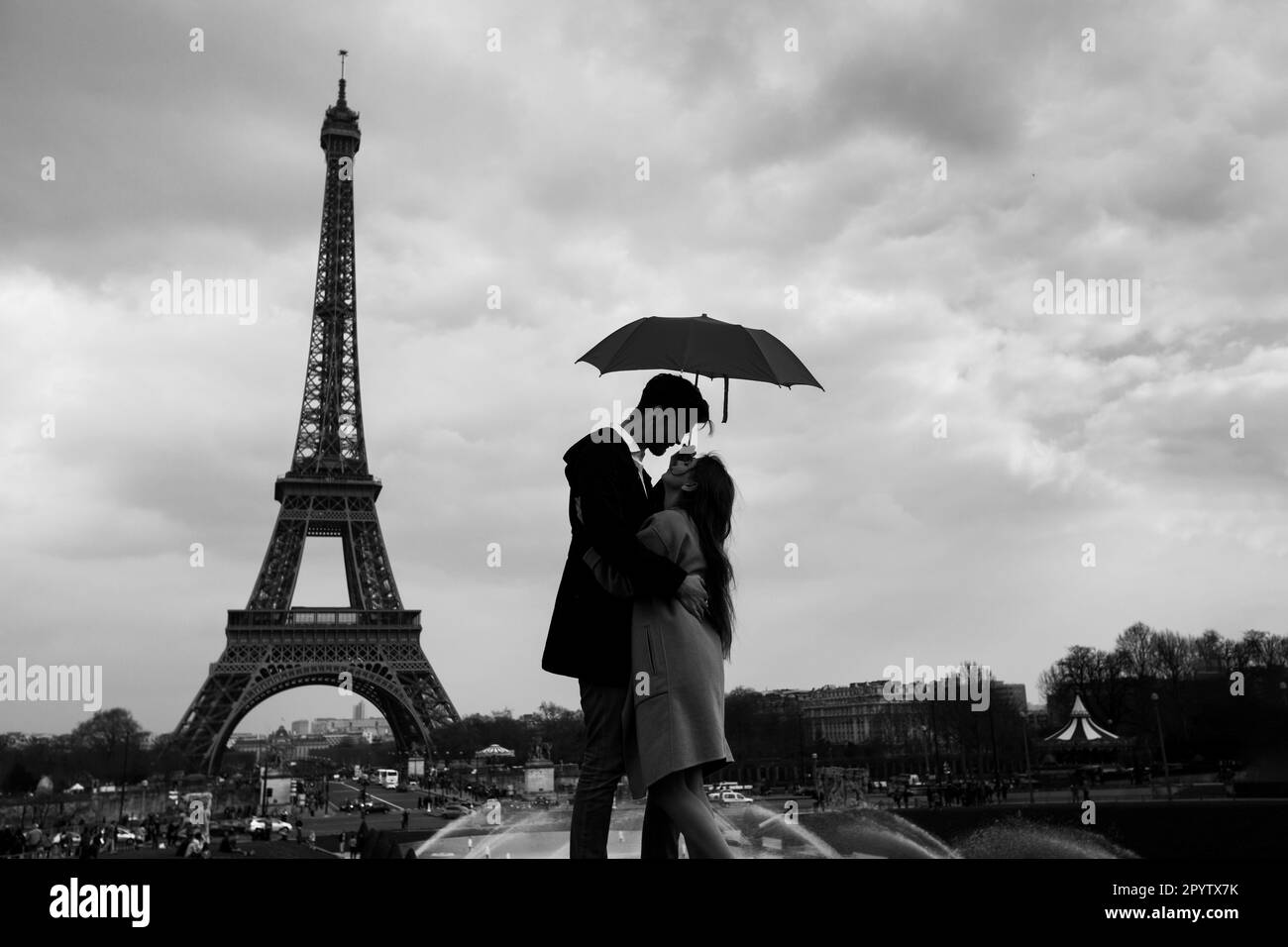 Retro-Blick auf Paris, Paar unter dem Schirm in der Nähe des Eiffelturms, klassisches Schwarz-Weiß-Schwarz Stockfoto