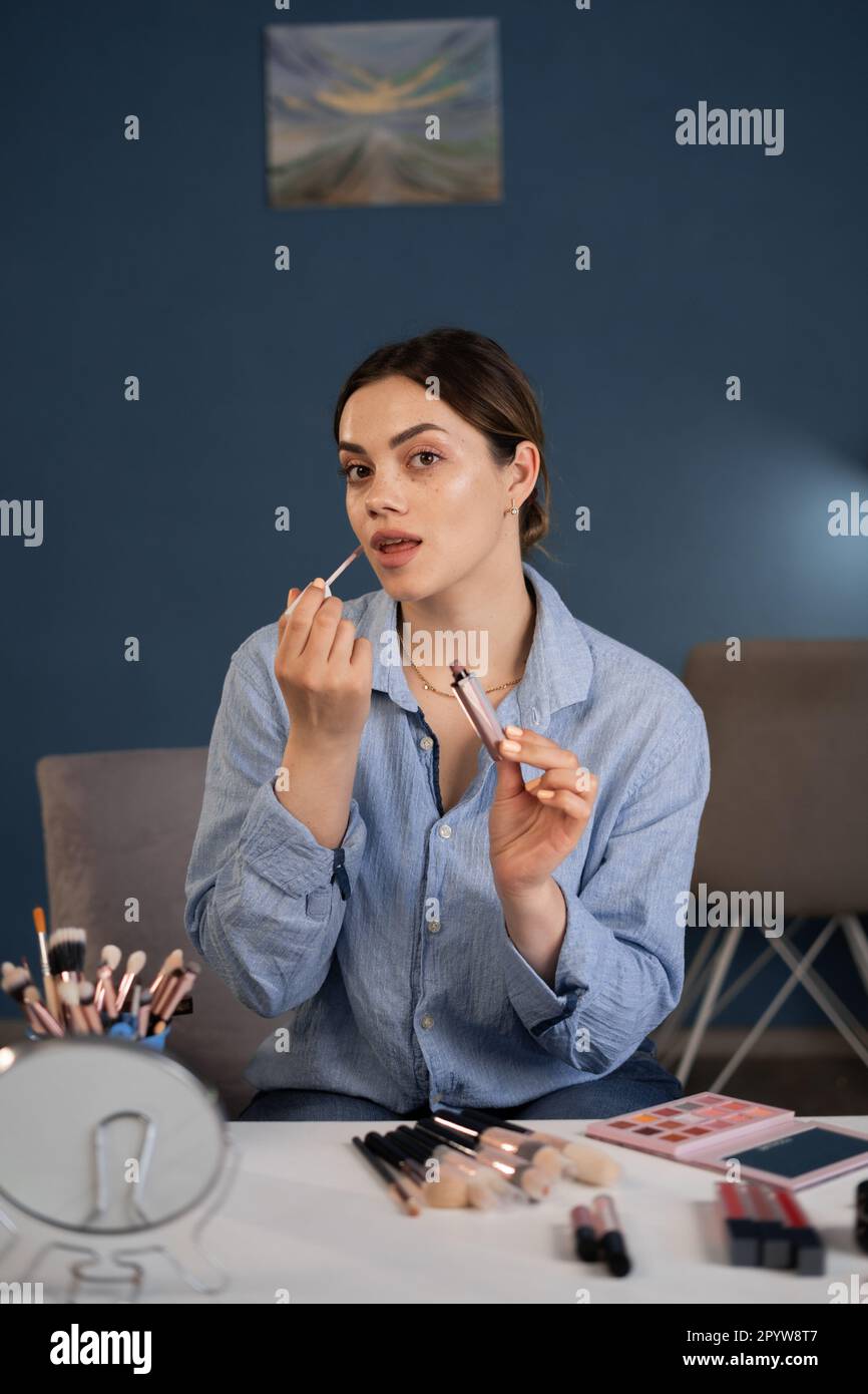 Eine junge Frau, die über Kosmetika spricht und dabei einen Lippenstift hält, während sie ihr Video aufnimmt, und ein Video für ihren Blog über Kosmetik macht. Stockfoto