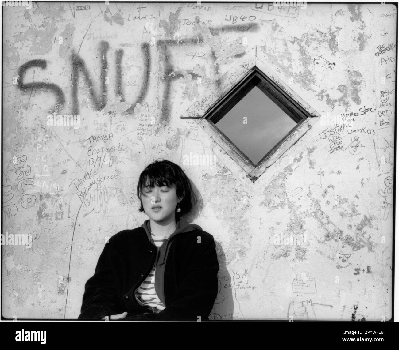 Dublin, Irland. Ethnologie, Graffiti, Bushaltestelle. Japanische Touristen sonnen sich vor einer Mauer mit dem Graffiti „SNUFF“. Schwarz-Weiß. Foto, 1992. Stockfoto