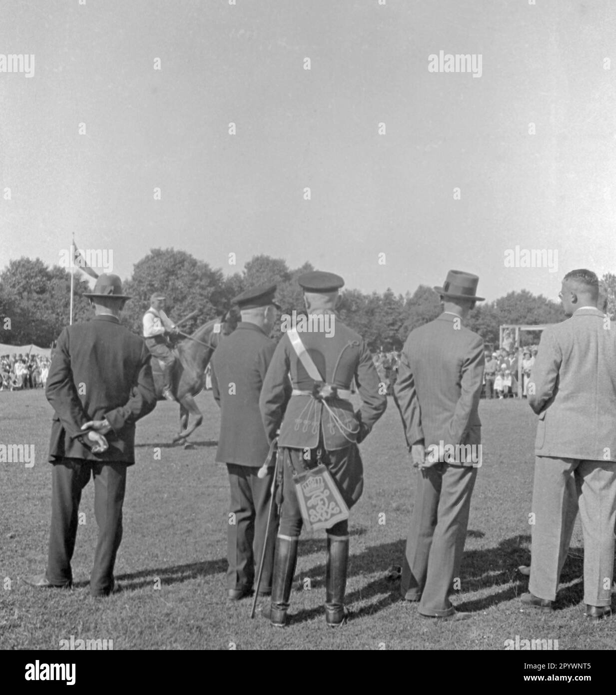 Zuschauer sehen den Ring in Warnemünde. Beim Ringfahren wird eine Lanze durch einen Ring gesteckt, der an einem Gerüst hängt. Der Mann in der Mitte trägt eine Uniform der preußischen Armee. Stockfoto