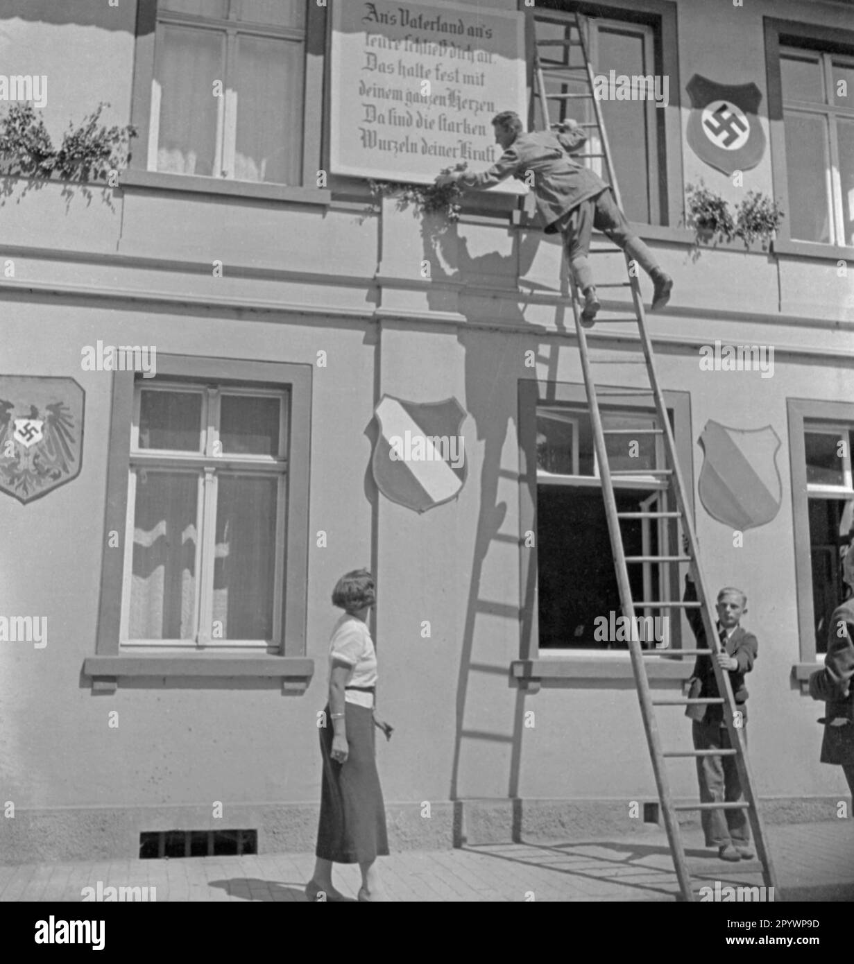 Die Häuser werden anlässlich des Treffens der Mecklenburger Einwohner in Laage dekoriert. An der Fassade sind die Farben schwarz-weiß-rot, rechts Mecklenburg gelb-rot-blau. Oben rechts ein Schild mit Hakenkreuz. Stockfoto