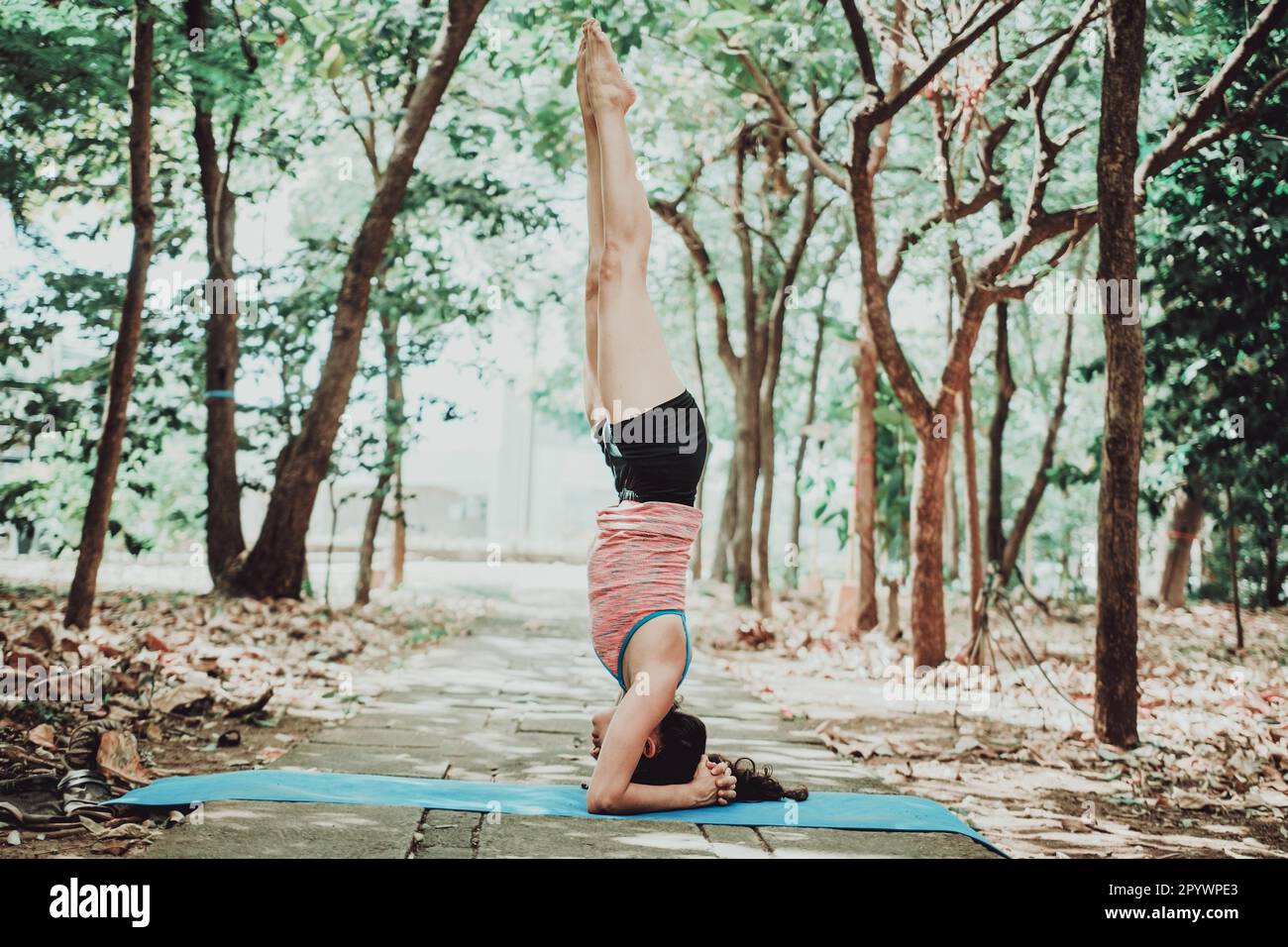 Junge Frau, die im Freien Yoga am Kopfständer macht. Spirituelles Mädchen, das draußen Yoga sirshasana praktiziert Stockfoto