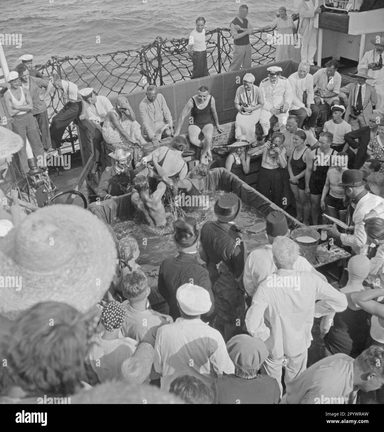 Passagiere bei einer Kreuzungszeremonie auf dem Oberdeck eines Passagierschiffs der Monte-Klasse. In der Mitte macht eine Frau Fotos von der Szene mit einer Contax I. Die Schiffe der Monte-Klasse gehörten der Hamburger Südamerikanischen Dampfschifffahrts-Gesellschaft KG und waren seit 1924 auf der Strecke von Hamburg zur Ostküste Südamerikas unterwegs. Stockfoto