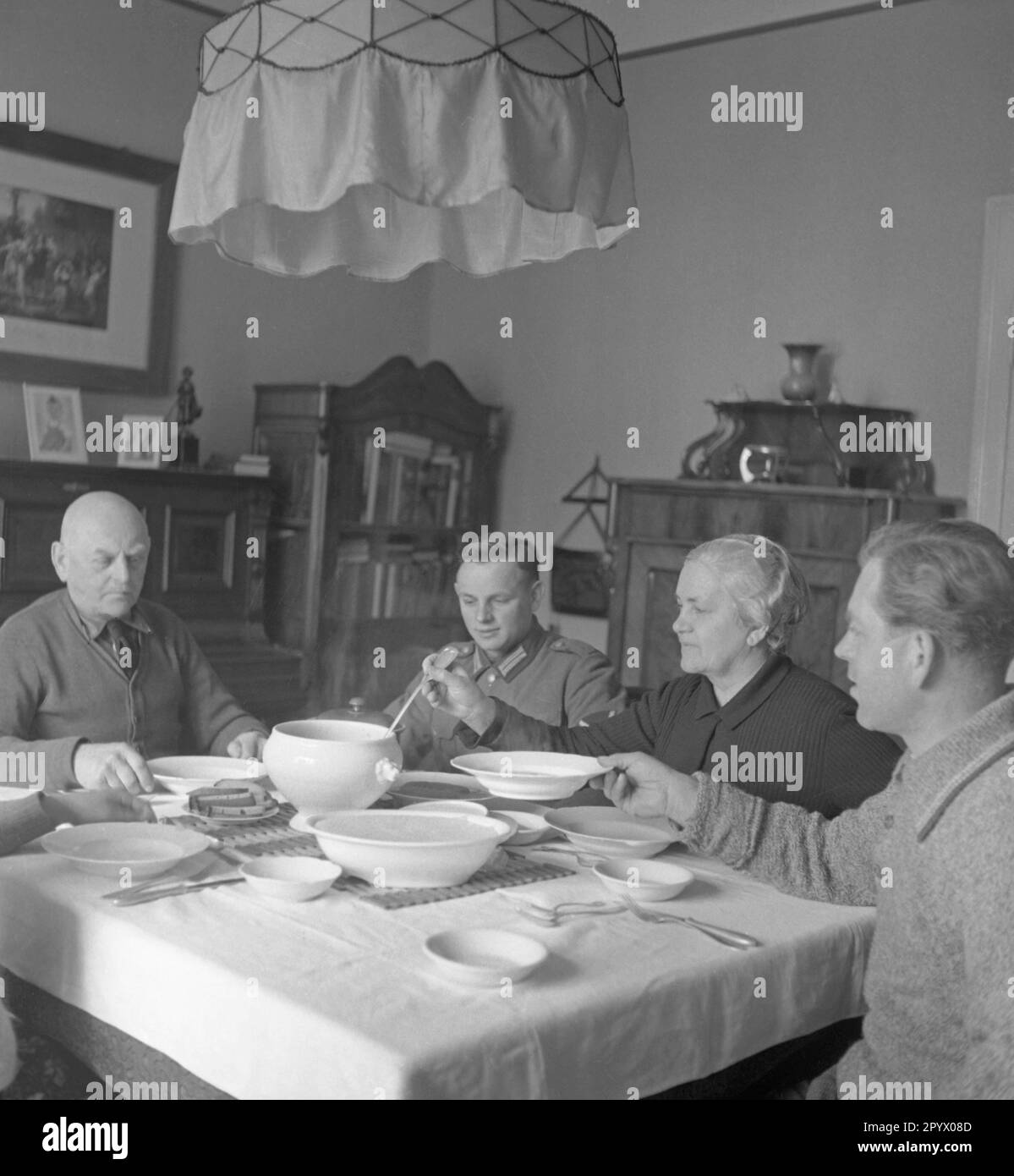 Fünf Leute sitzen an einem überdachten Esstisch, wahrscheinlich auf einer Farm in der Nähe von Neustrelitz. Eine Frau verteilt Essen aus einer Suppenschüssel. Unbefristetes Foto. Stockfoto