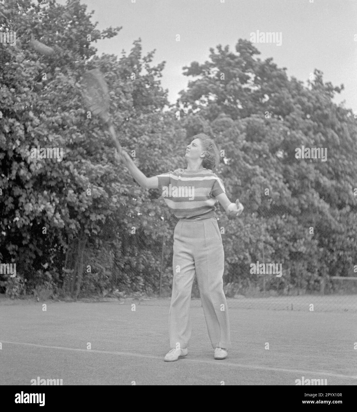 Eine Frau mit langen Hosen und gestreiftem T-Shirt schlägt beim Badminton auf den Ball. Stockfoto